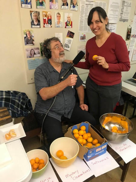 Marketplace reporter Mitchell Hartman offers a tangerine taste test to a participant at a holiday potluck and honey judging contest put on by Portland Urban Beekeepers. Credit: Mitchell Hartman